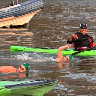 Two AGUA Masters team members swimming in a body of water with a person in a kayak smiling in the background