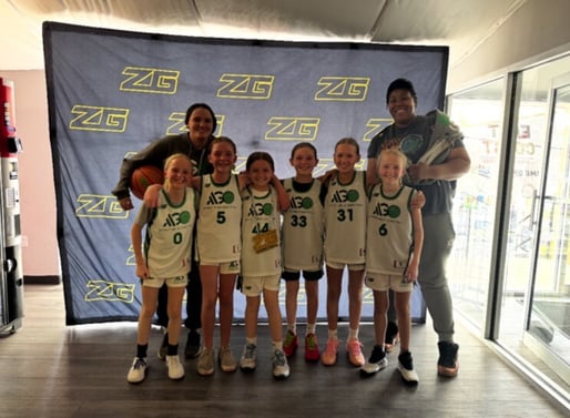 Asphalt Green Basketball Program's fourth grade girls team smiling in front of a step and repeat with their coaches4th grade- chip
