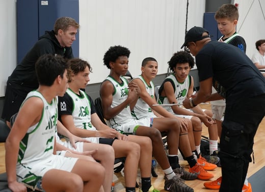 Asphalt Green Basketball Program's eighth-grade boys team sitting on a bench talking to their coach.