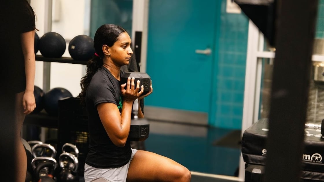 A person performs a dumbbell lunge exercise in a gym.