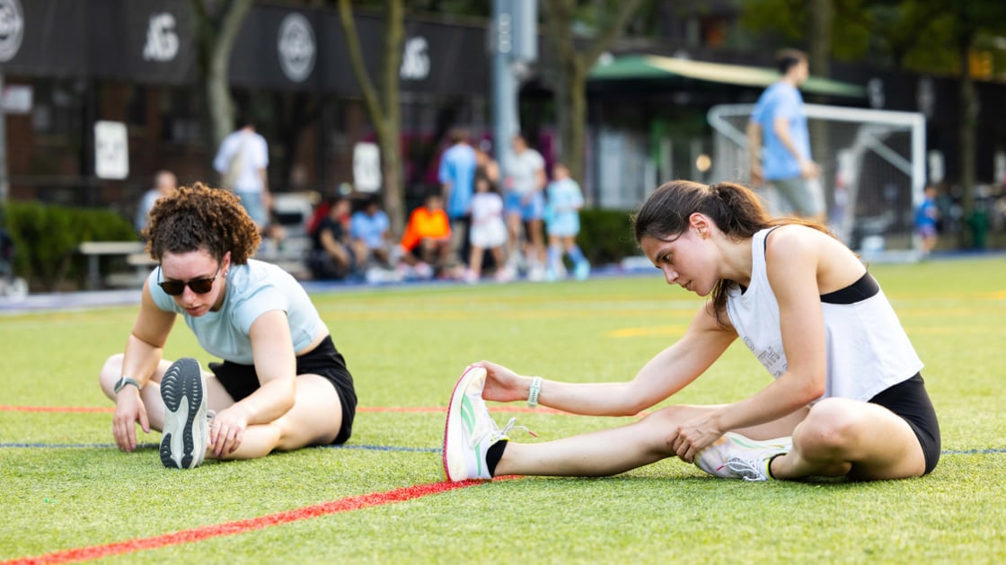 Two people stretching on Litwin Field before an outdoor HIIT class.